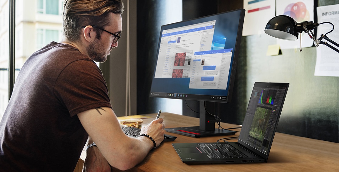 Young white guy sitting in front of a monitor, keyboard, and Lenovo ThinkPad X1 Extreme Gen 4 laptop.